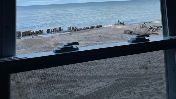 Blick auf den Strand von innerhalb eines Gebäudes aus, mit blauem Himmel und ruhiger See.
