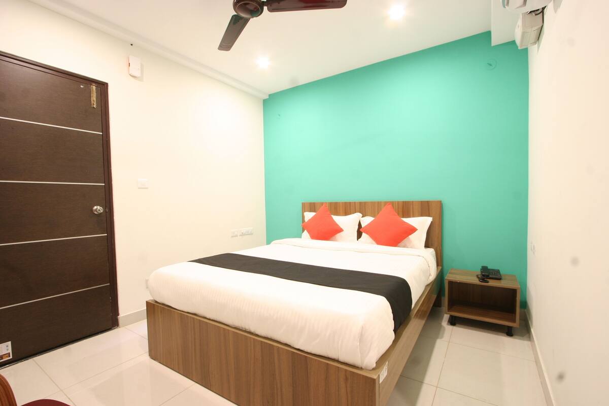 A bedroom with a bed, a nightstand, a wooden wardrobe, and a teal-colored wall.