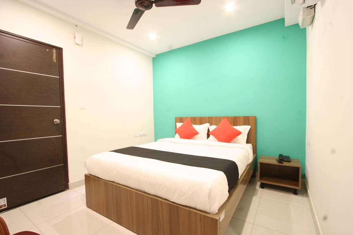 A bedroom with a bed, a nightstand, a wooden wardrobe, and a teal-colored wall.