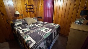 A wooden-paneled room with a bed, a nightstand, a lamp, and a window with curtains. - #6 Miami Beach Resort  (Au Sable Charter Township)