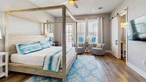 Un lit à baldaquin avec un cadre en bois et une couvre-lit bleue et blanche, un ventilateur de plafond et une grande fenêtre avec des stores.