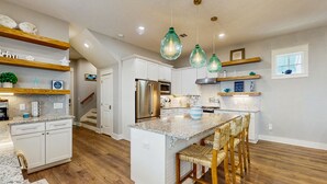 Une cuisine moderne avec des meubles blancs, un îlot central et des suspensions vertes.