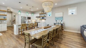Une cuisine spacieuse dotée d’un îlot central, d’une table à manger en bois et de chaises. On y trouve des luminaires suspendus et un lustre.