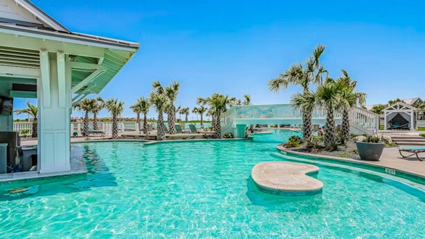 Une piscine d’eau cristalline, bordée de palmiers et dotée d’un espace abrité.