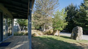 Una terrazza in legno coperta con vista su un giardino curato, che include una roccia grande e alberi.
