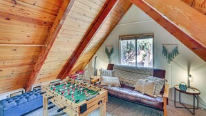 Ein gemütliches Schlafzimmer im Loft-Stil mit Holzbalkendecke, einem Tischkicker, einem Ledersofa und einem Fenster mit Blick auf Bäume.