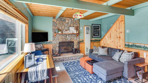 Ein gemütliches Wohnzimmer mit einem Kamin aus Stein, einem grauen Sofa und einer Holzbalkendecke.