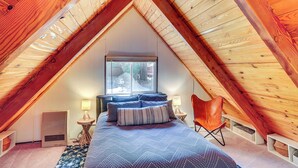 Ein Schlafzimmer mit schrägen Wänden, einem Bett mit blauer Bettwäsche, einem Fenster und einem Heizgerät.