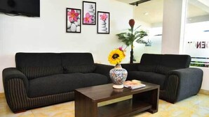 A living room with a dark sofa, a wooden coffee table, and a vase with flowers. - PPH Living Bhimas (Tada)