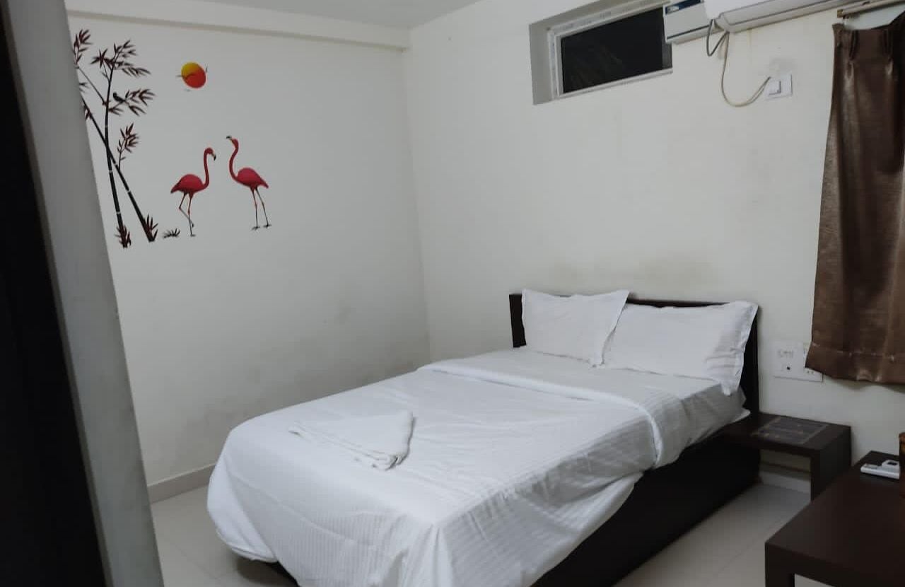 A single bed with white bedding, a small bedside table, and a wall decoration of flamingos and bamboo.