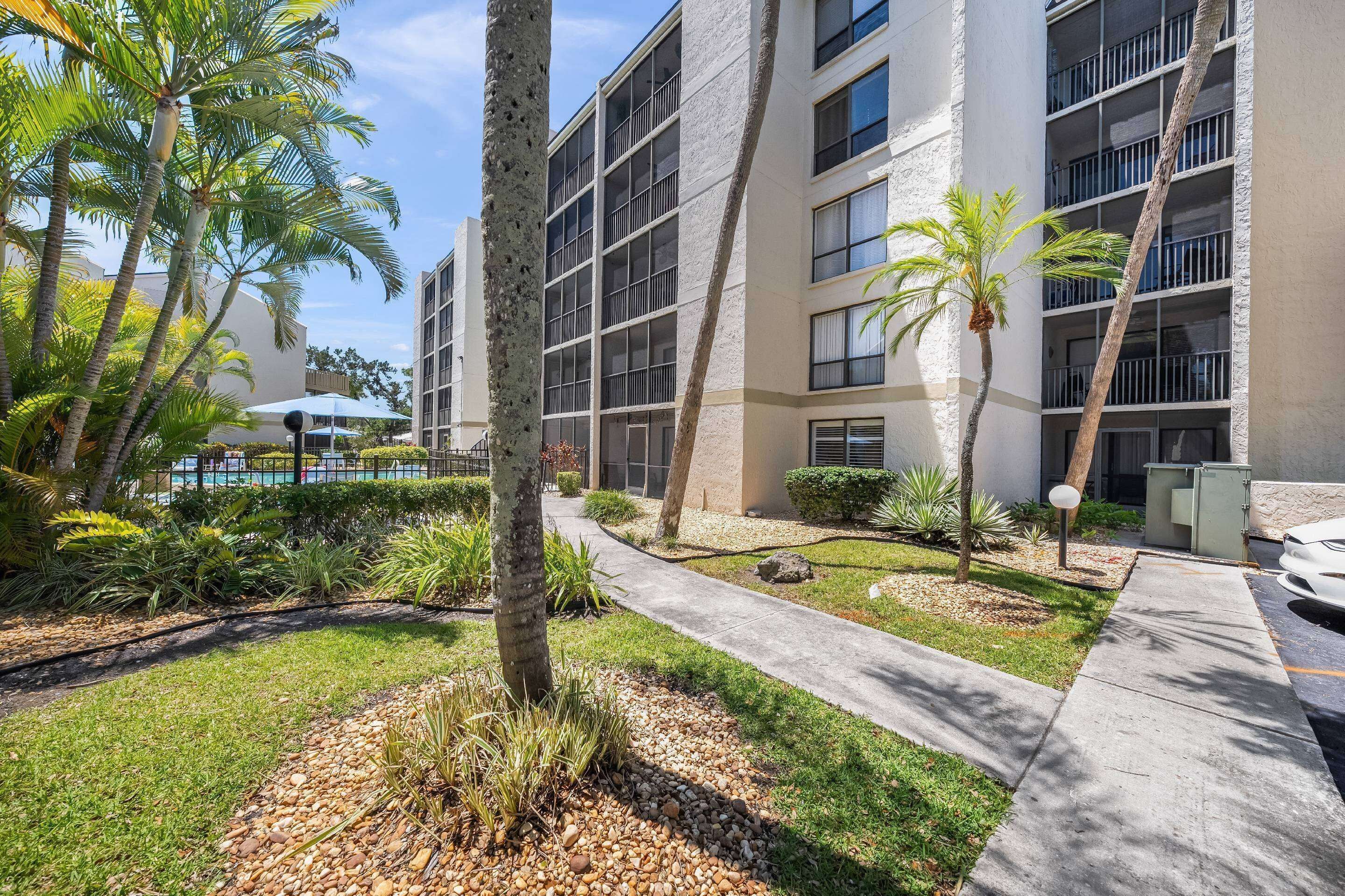 A multi-story building with balconies, surrounded by palm trees and a pathway.
