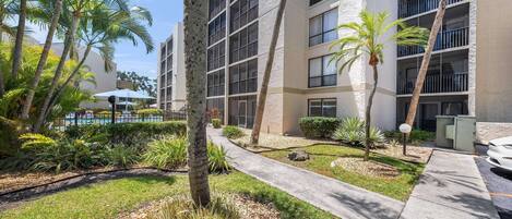 A multi-story building with balconies, surrounded by palm trees and a pathway.