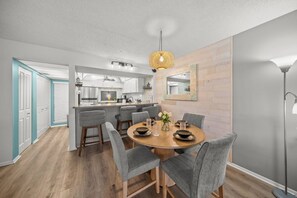 A modern kitchen with a central island, grey upholstered chairs, and a round wooden dining table.