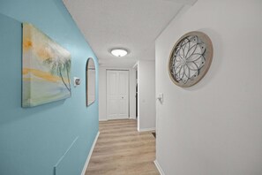 A hallway with a light blue wall, a wooden floor, a white door at the end, and a decorative metal piece on the right wall. - Peaceful Bayfront Retreat at Siesta Key's Bay Oaks (Siesta Key)