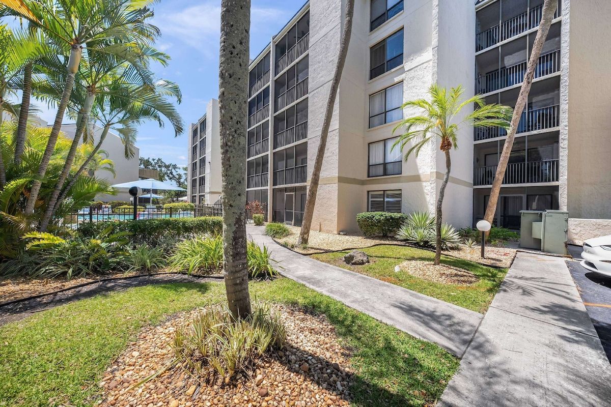 A multi-story building with a pool area, palm trees, and a well-maintained garden.
