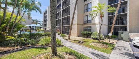 A multi-story building with a pool area, palm trees, and a well-maintained garden.