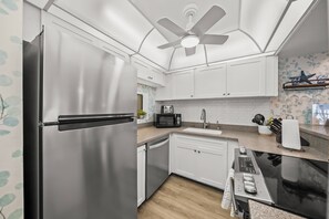 A modern kitchen with stainless steel appliances, white cabinets, a ceiling fan, and a backsplash with a leaf pattern.