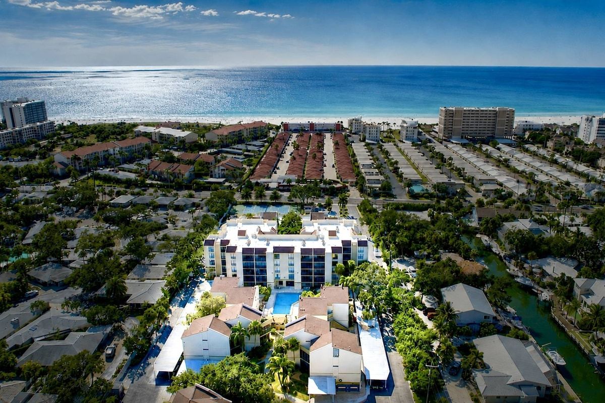 Un complexe hôtelier doté d’une piscine centrale, entouré de villas et offrant une vue sur la plage.