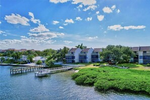 A waterfront property with a dock, lush greenery, and multi-story buildings.