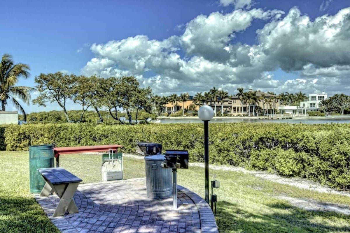 A paved outdoor area with a bench, trash bins, and a lamp post.