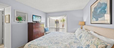 Een slaapkamer met een bed, een dressoir, een televisie en kunstwerken.