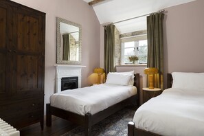 A bedroom with two beds, a wooden wardrobe, a fireplace, and a window with curtains. - Family friendly holiday cottage in the Cotswolds with a superb garden - Winterberry Cottage (Barnsley, near Cirencester)