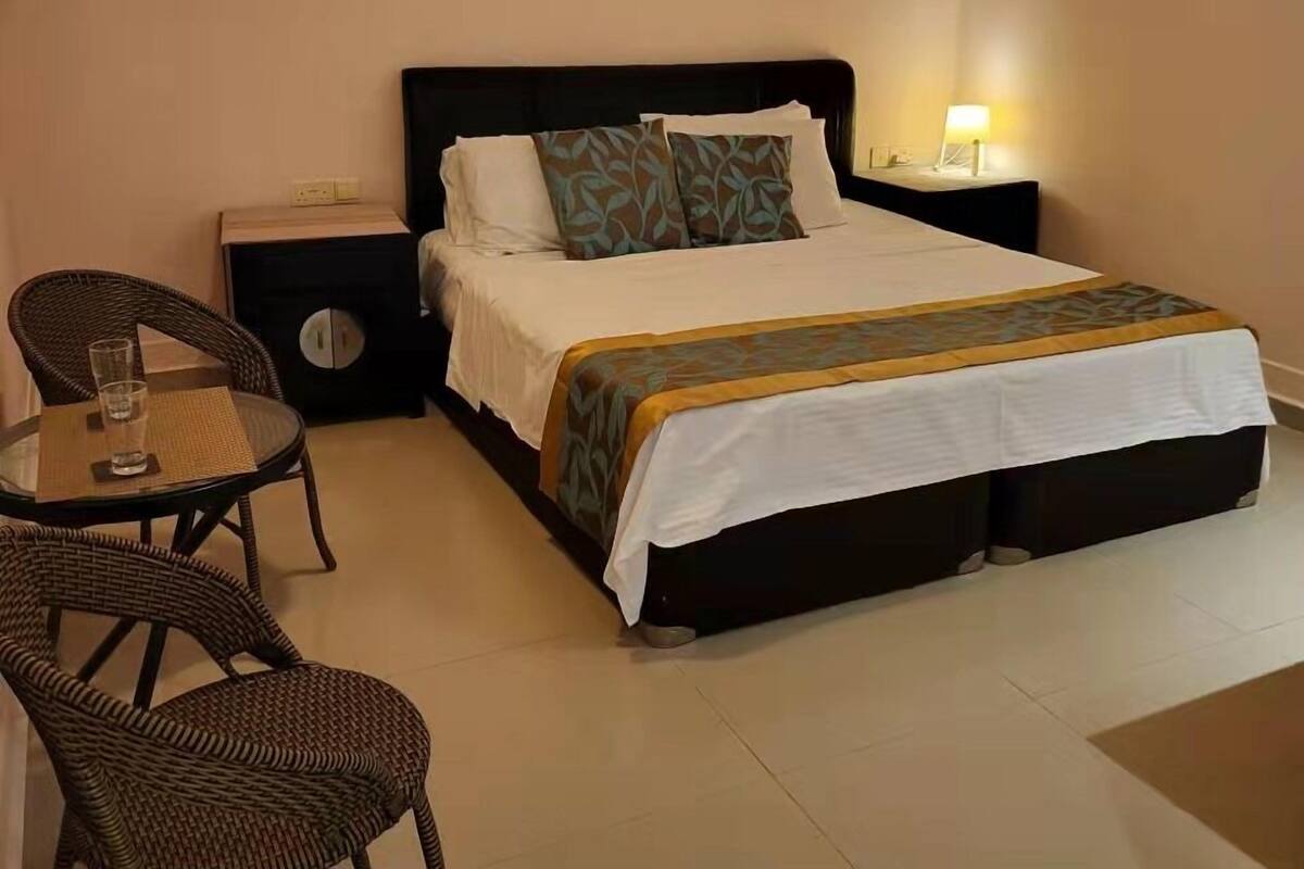 Ein Hotelzimmer mit einem Bett, einem Nachttisch, einer Lampe und zwei Korbstühlen.