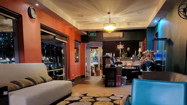 Een hotel lobby met een bank, een blauwe stoel, een kamer met een patroon en een bar op de achtergrond.