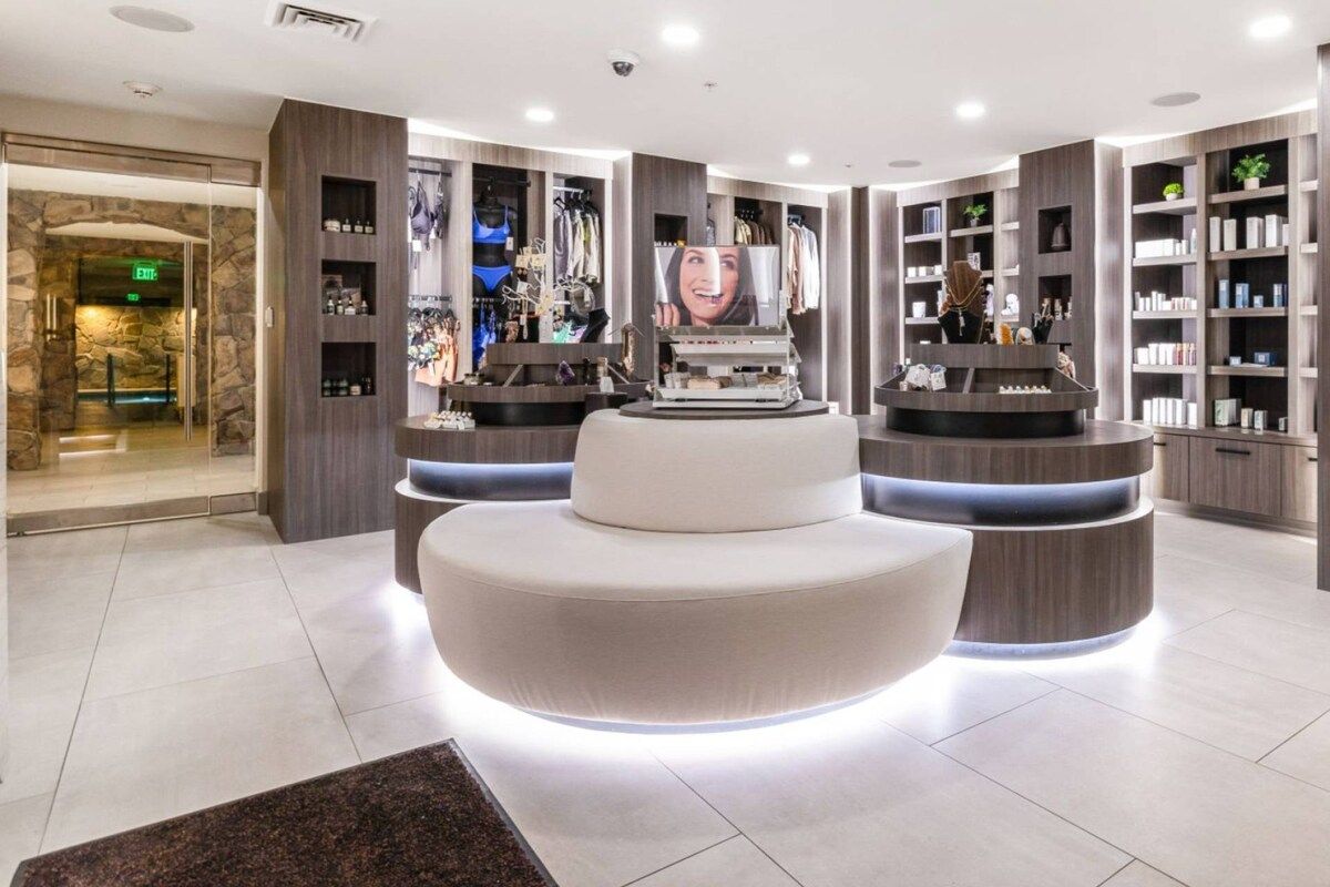 A modern lobby with a central seating area, a reception desk, and a wall with shelves displaying various items.