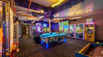 An indoor arcade with various gaming machines, a pool table, and neon signage.