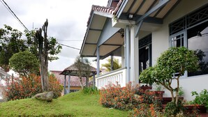 A house with a covered porch, a small garden with red flowers, and a tree. - Classic Herman by Broga (Cipanas)