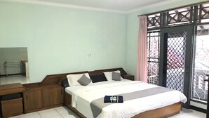 A bedroom with a bed, wooden nightstands, a desk, and a window with a metal gate. - Classic Herman by Broga (Cipanas)