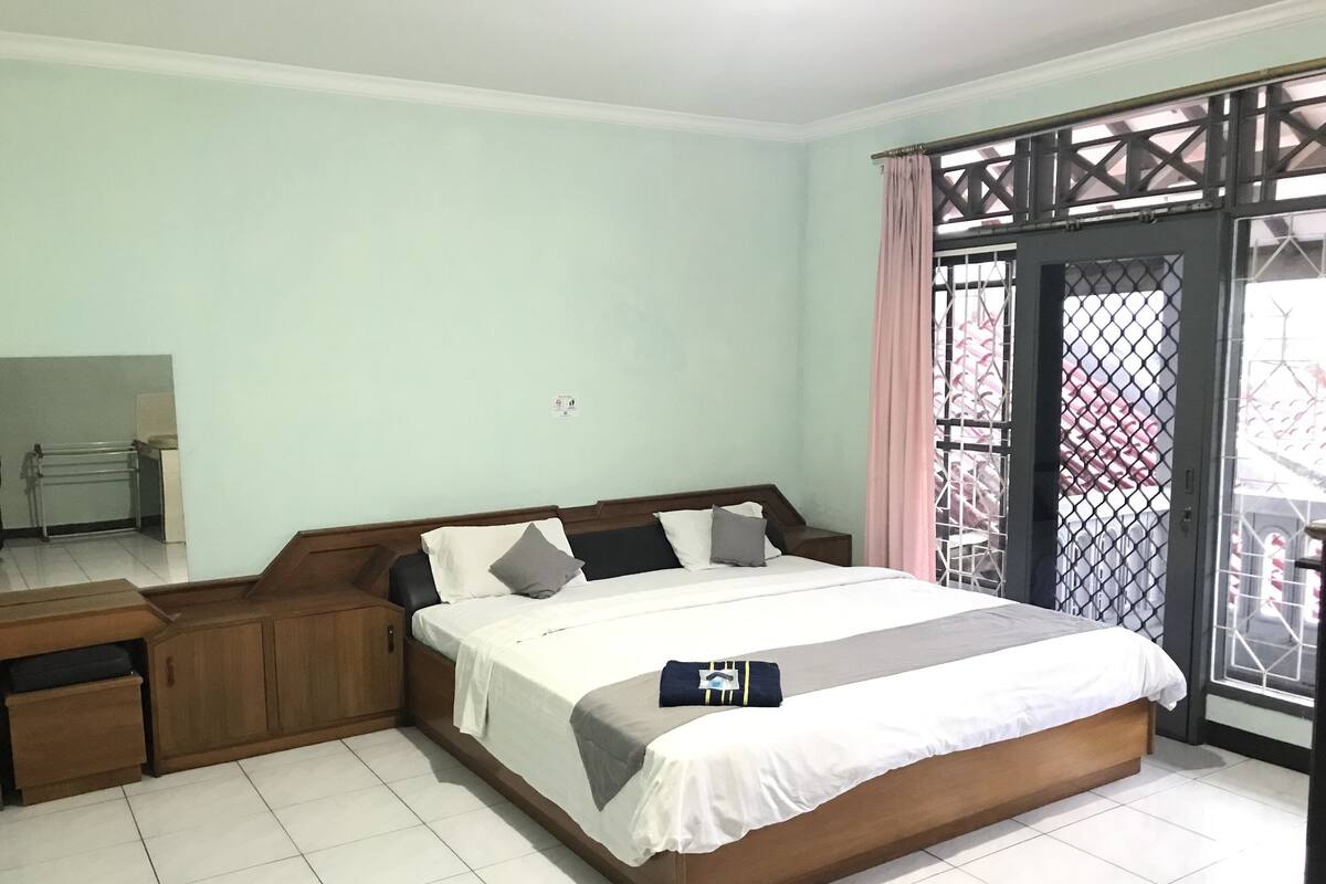 A bedroom with a bed, wooden nightstands, a desk, and a window with a metal gate.