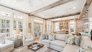 A spacious living room with a large sofa, a coffee table, and a dining area with wooden cabinets and pendant lights.