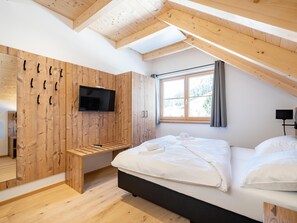 A bedroom with a sloped ceiling, wooden walls, a bed, a TV, and a window with a view of trees. - Detached chalet with sauna by a stream (Donnersbachwald)