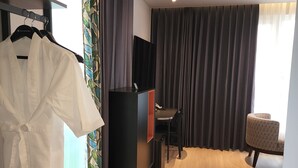 A hotel room with a wooden floor, a TV on a stand, a desk with a chair, and a wardrobe with a robe hanging. - Jinhae InterCity Hotel (Changwon)