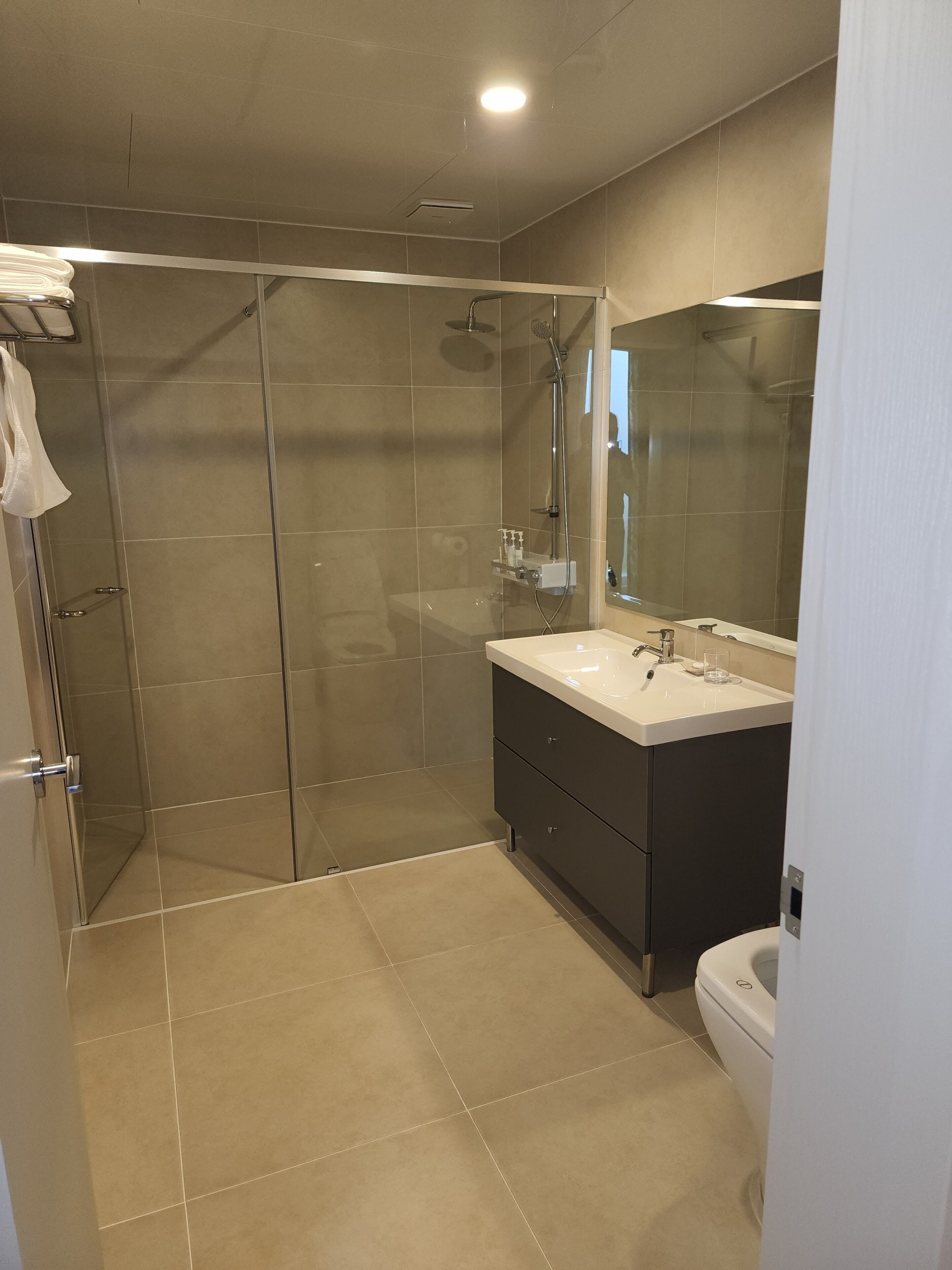 Un baño moderno con ducha envuelta en vidrio, tocador con espejo y retrete.