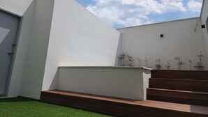 A modern building with a flat roof, a set of wooden steps leading up to a white wall, and a small garden area with artificial grass and a few plants. - Jinhae InterCity Hotel (Changwon)