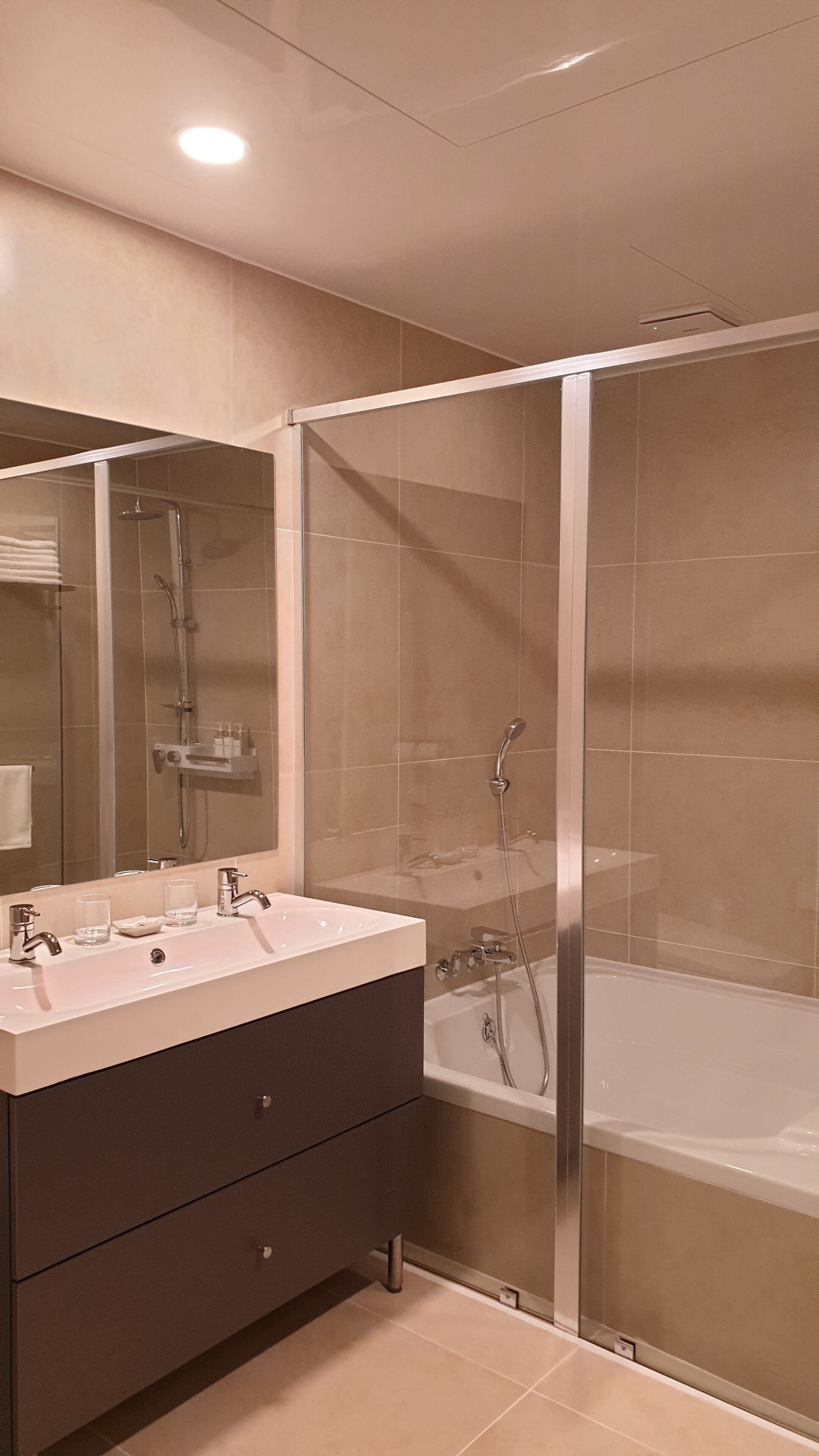 A modern bathroom with a glass-enclosed shower, a double sink vanity, and a bathtub.