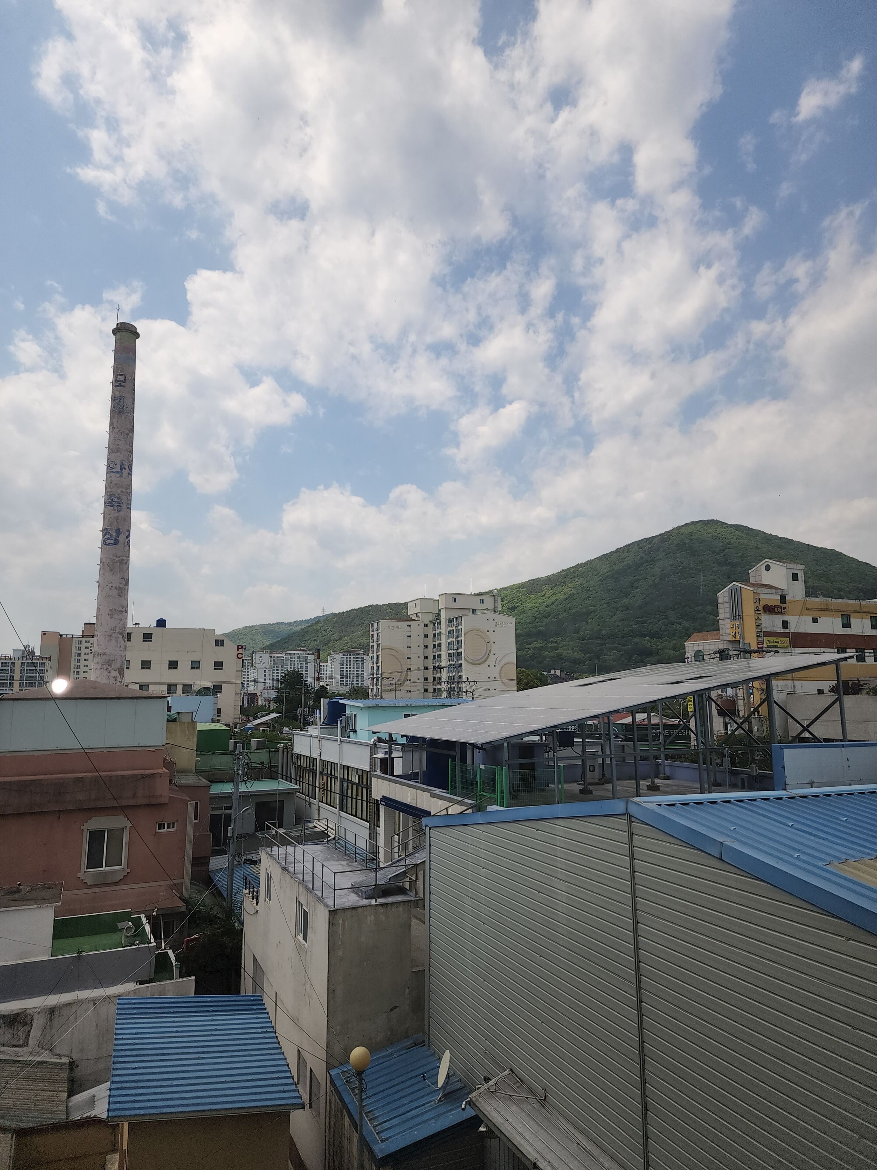 A view of a residential area with buildings, a tall chimney, and a hill in the background.