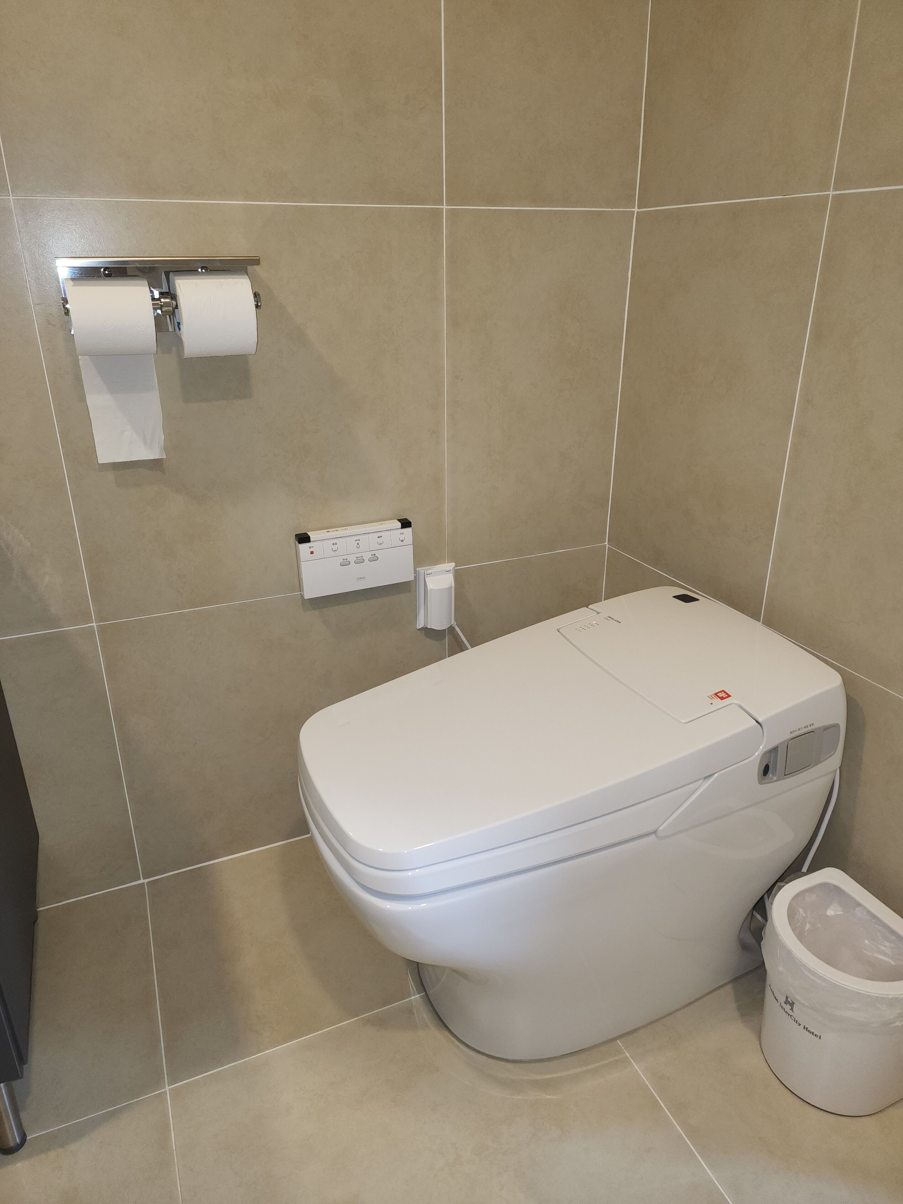 A modern bathroom with a toilet, a paper towel dispenser, and a trash bin.