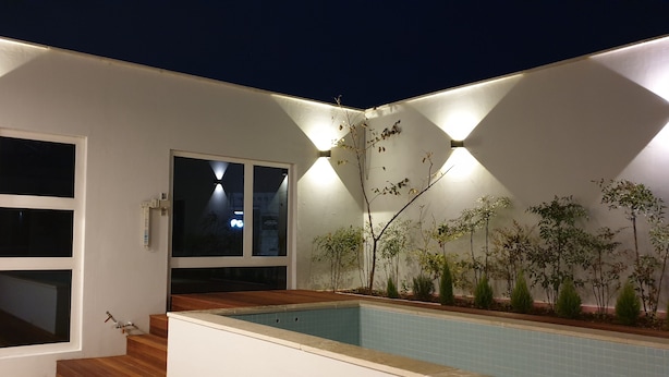 A modern outdoor pool area with a wooden deck, a small pool, and a white wall with built-in lighting. - Jinhae InterCity Hotel (Changwon)