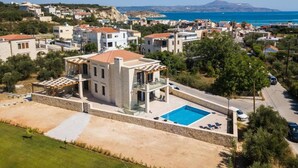 Una vila moderna amb piscina, envoltada d'un paisatge verdós i vistes al mar.