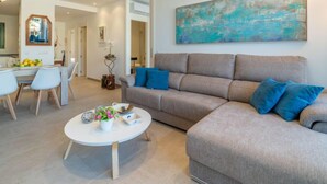 Ein modernes Wohnzimmer mit einem grauen Sofa, blauen Kissen, einem weißen Couchtisch mit Blumen und einem großen abstrakten Gemälde an der Wand.