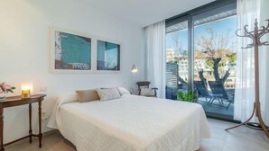 Ein Schlafzimmer mit einem großen Bett, einem Nachttisch, einer Lampe und Blick ins Freie durch eine Schiebetür.