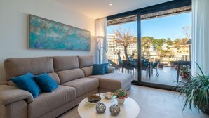 Ein modernes Wohnzimmer mit einem beigefarbenen Sofa, einem runden Couchtisch und einem großen Fenster mit Blick auf eine Wohngegend.