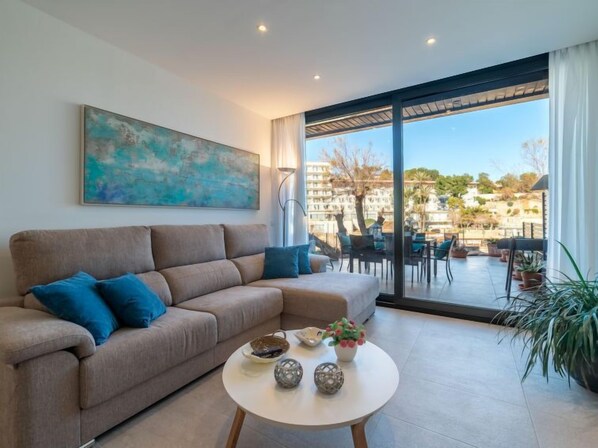 A modern living room with a beige sofa, a round coffee table, and a large window offering a view of a residential area.