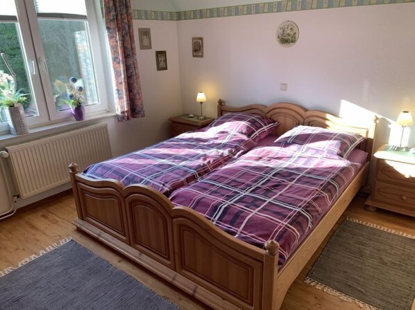 Une chambre à coucher avec un lit en bois, deux tables de chevet, une fenêtre avec des rideaux, un radiateur et une horloge fixée au mur.