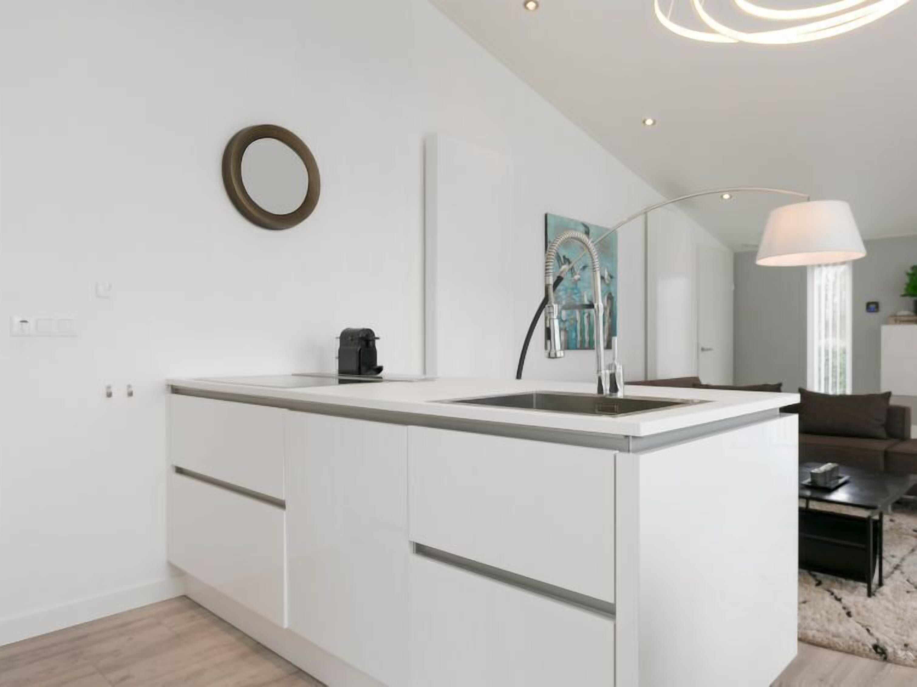 Una cocina moderna con una isla central, armarios blancos y un lavamanos de acero inoxidable.