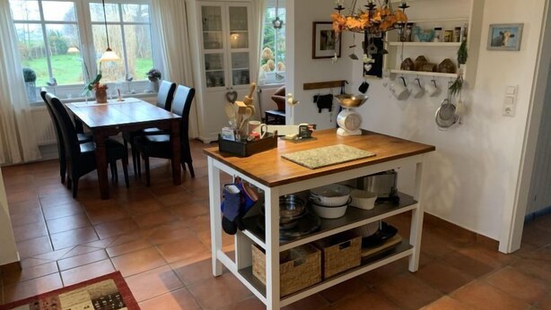 Eine Küche mit Holztisch und -stühlen, einer Hängeleuchte und Regalen mit Küchenutensilien.